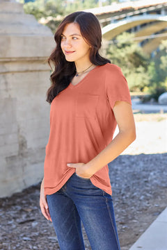 Woman wearing a rust-colored top and blue jeans standing outdoors.