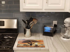Glass cutting board with elephants and trees design sitting on kitchen counter next to a gas stove