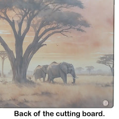 Two elephants under a large tree in a savanna setting on the back of a cutting board.