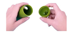 Two hands holding green silicone pet waste dispenser open with lid in right hand and container in left, against a white background