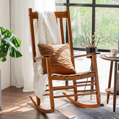 Wooden rocking chair with a pillow and blanket in a bright room with a window.