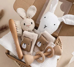 Collection of baby toys including a wooden brush, knitted rabbit, and teething rings on a neutral background.