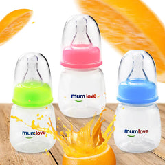 Three baby bottles with colourful caps and 'mumlove' branding on a wooden surface with orange juice splashes.