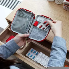 Person opening a red and gray first aid kit on a wooden surface with medications visible.