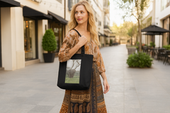 using gid://shopify/MediaImage/41377699692848, please create an image of a blonde woman walking through a shopping Plaza carrying this tote over her shoulder with the design clearly visible. She should be wearing a bohemian style skirt and blouse.