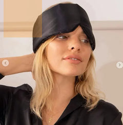 Woman wearing a black silk sleep mask against a neutral background