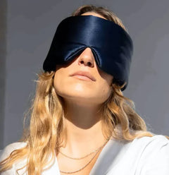 Person wearing a black silk sleep mask against a neutral background